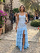 Woman in a light blue dress standing outdoors with decorative elements and people in the background.