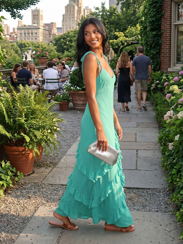 Front view of elegant emerald green chiffon maxi dress showcasing the soft V-neckline, self-tie shoulder straps, and fluid cascading ruffles in a luxurious European estate parlor.