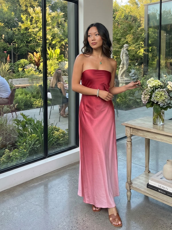 Front view of elegant burgundy to blush pink ombre satin strapless evening gown, showcasing the sleek minimalist fit and rich liquid fabric texture in a glass-walled garden patio.