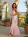 Woman in a pink lace dress standing outdoors with potted plants and a scenic background.