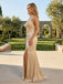 Woman in a beige evening gown standing outdoors with greenery and stone arches in the background