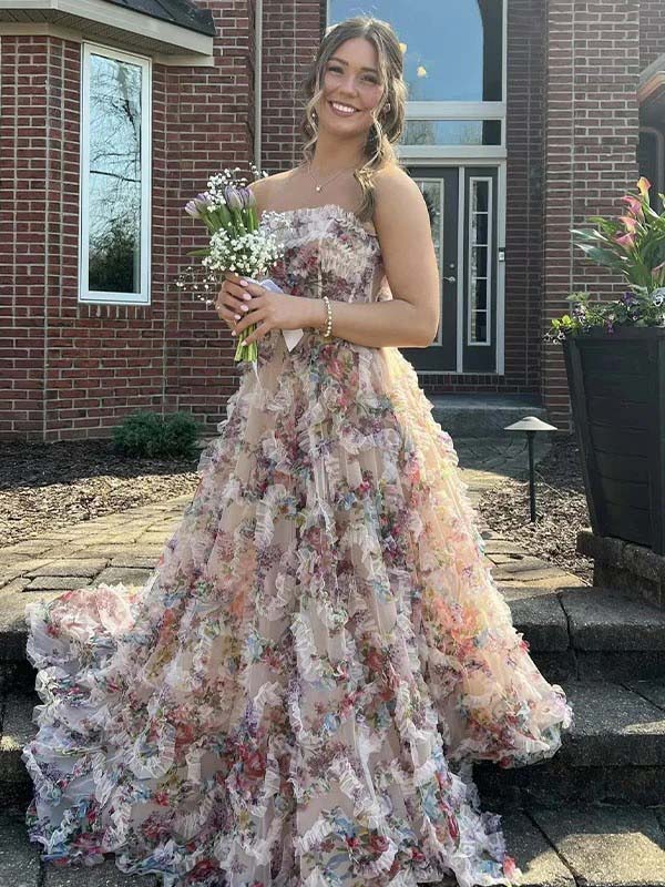 Woman in a floral dress holding flowers in front of a brick building.