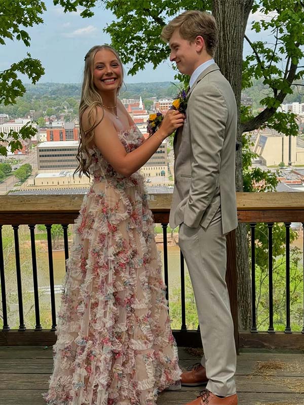 Two people in formal attire standing on a balcony with a scenic city view.