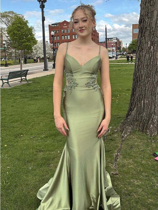 Woman in a green evening gown standing outdoors on grass with buildings in the background