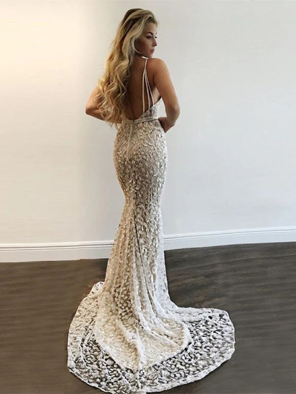 Woman wearing a white lace mermaid gown against a plain wall.