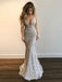 Woman wearing a white lace evening gown against a plain wall.